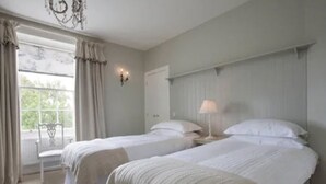 Ein Schlafzimmer mit zwei Betten, einem Fenster mit Vorhängen, einer Chandelüster und einem Nachttisch mit Lampe.