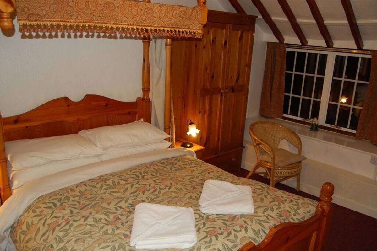 A bedroom with a wooden bed, a nightstand, a chair, and a window with curtains.