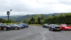 A parking lot with several cars, a signpost, and a view of rolling hills in the background.