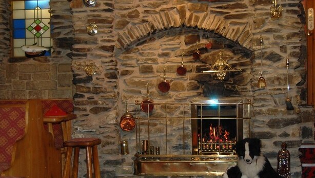 A stone fireplace with a dog sitting in front, wooden benches, and a clock on the wall.