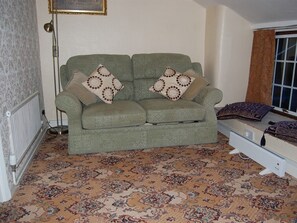 A living room with a green sofa, patterned cushions, a floor radiator, and a patterned carpet. - Britannia Inn (Llangollen)