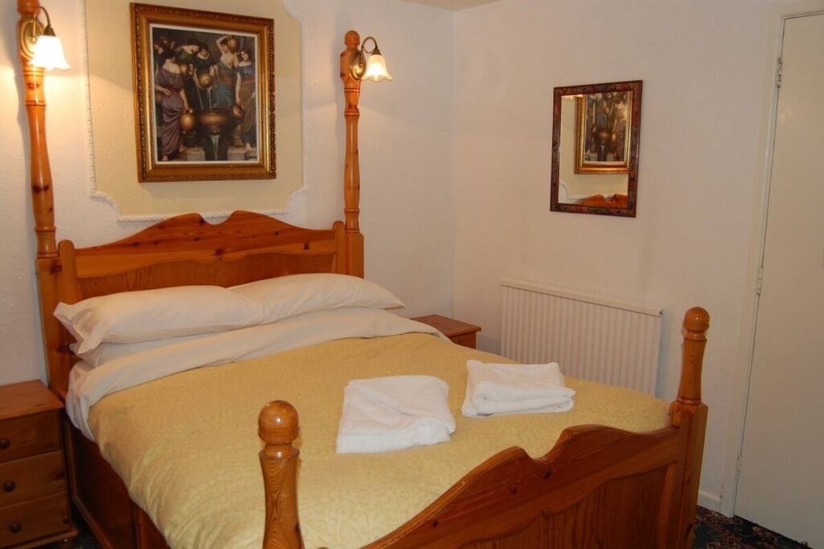 A wooden four-poster bed with white linens and towels, a nightstand, a lamp, and two framed pictures on the walls.