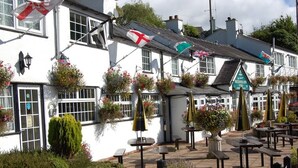 A traditional pub with outdoor seating, stone walls, and hanging flags.