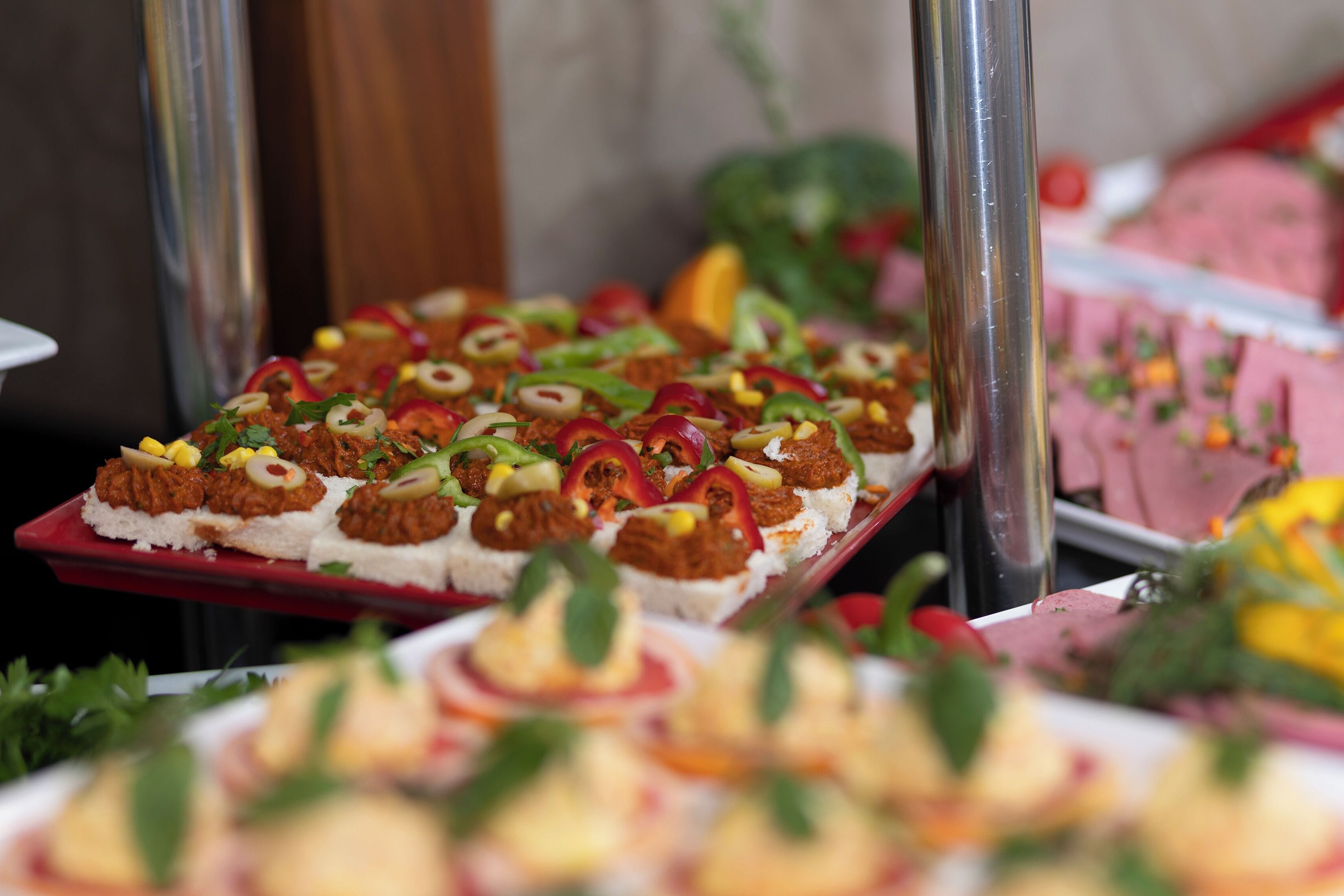 A buffet with various dishes, including a red tray with appetizers and a pink tray with meat dishes.