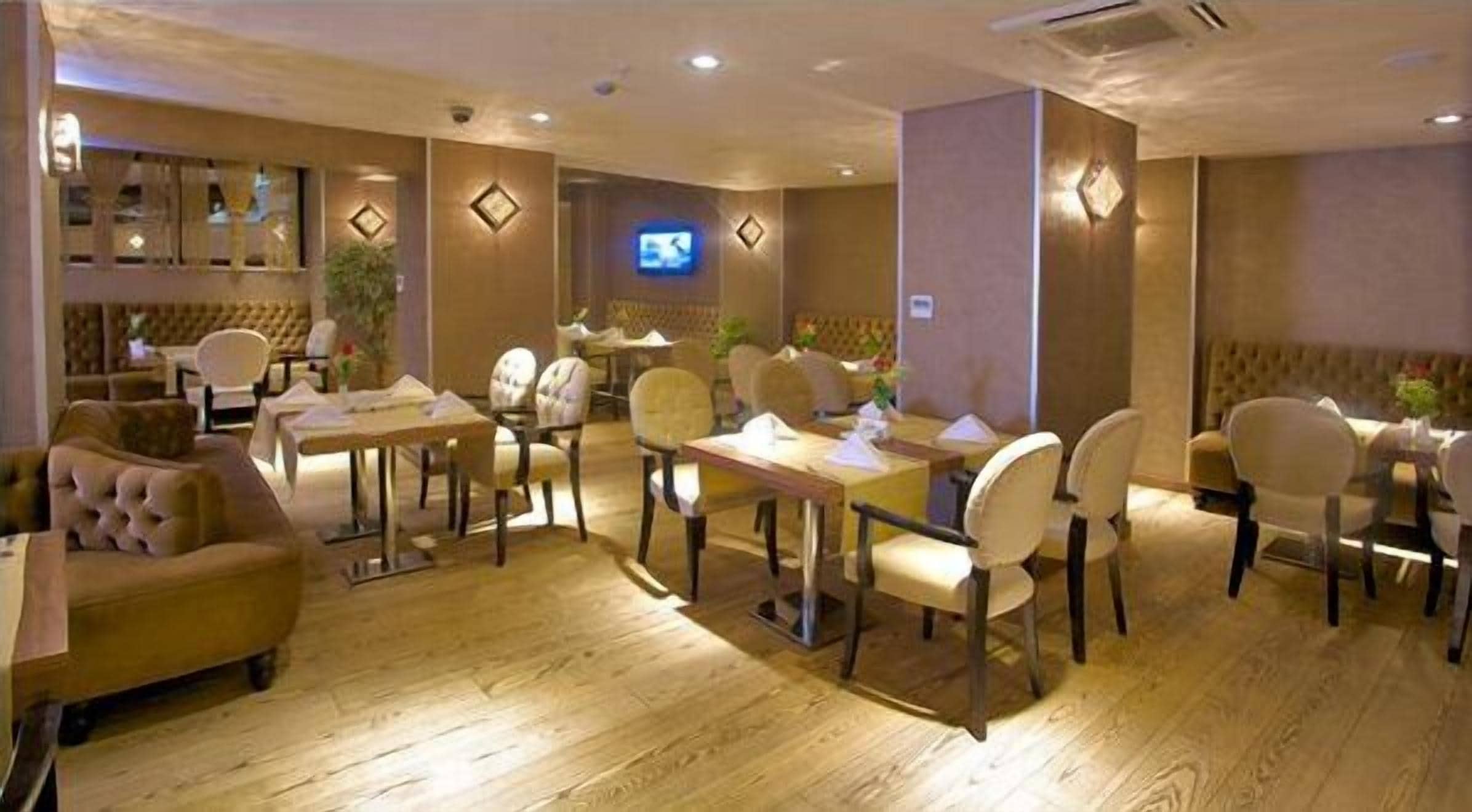 Un restaurante con suelo de madera, sillas acolchadas y mesas. Hay televisores montados en la pared e iluminación decorativa.