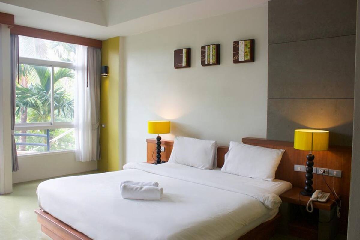 Habitación de hotel con una cama grande, dos lámparas de noche, un teléfono y una ventana con cortinas.