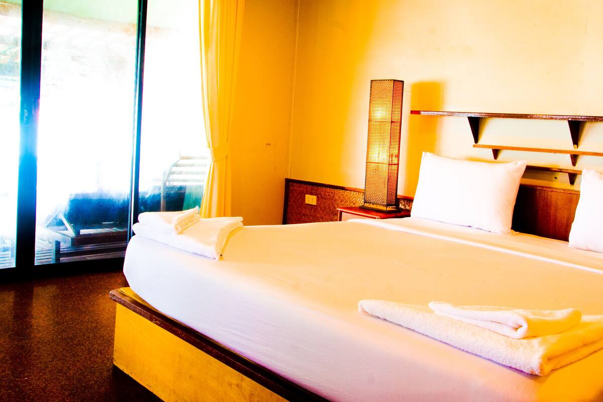 Habitación de hotel con una cama grande, una mesita de noche, una lámpara y vistas al exterior.