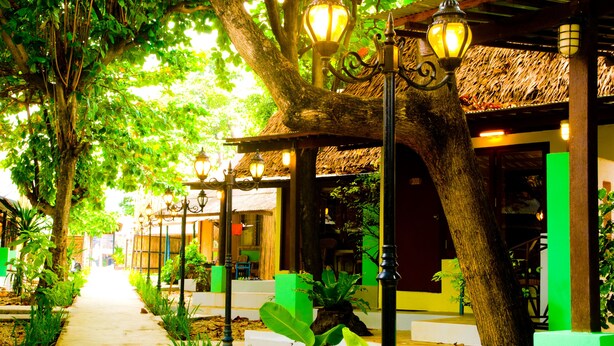 A pathway lined with trees and street lamps, leading to a building with a thatched roof and green walls. - Wimaan Buri Resort (Koh Samui)