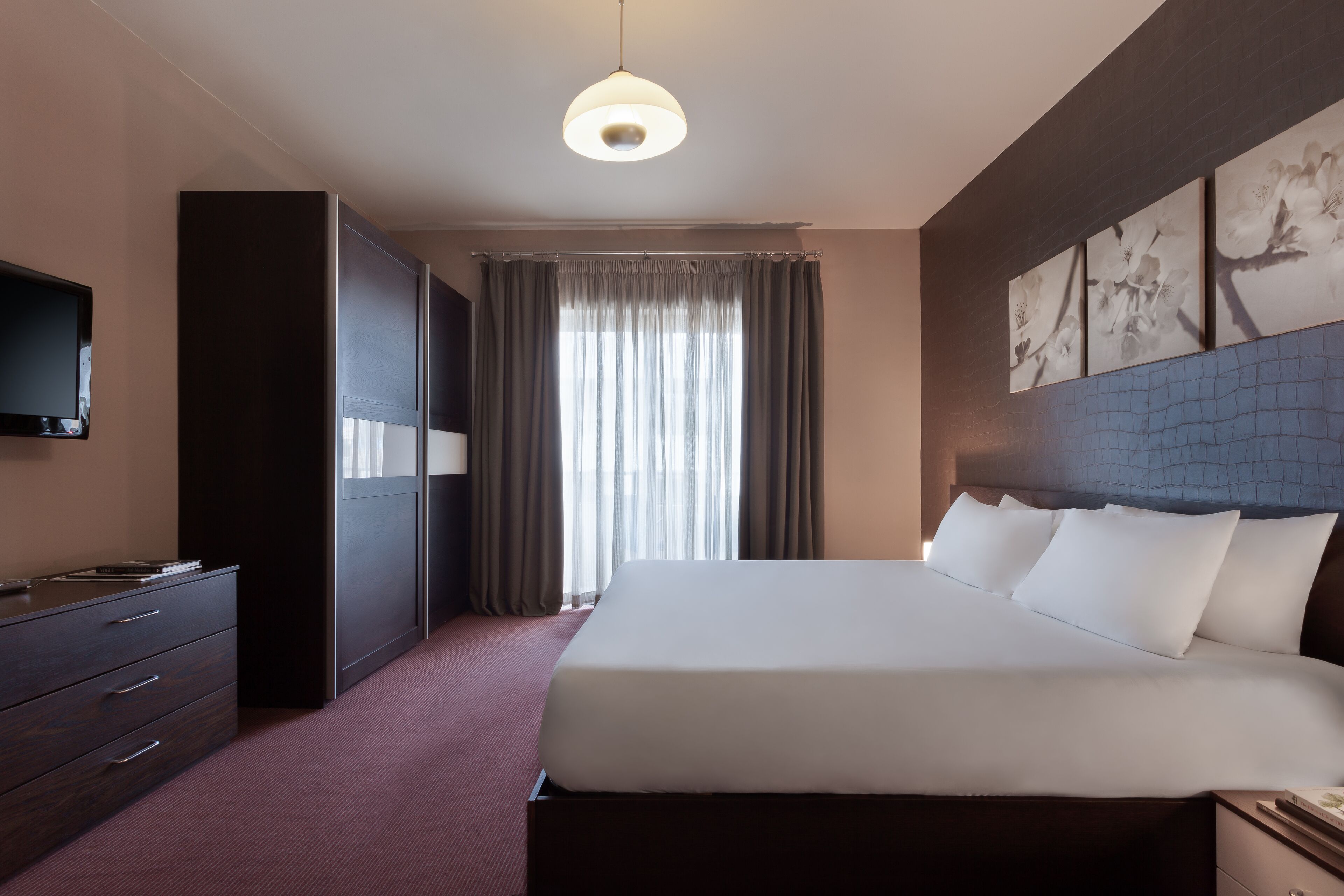 A hotel room with a large bed, a wardrobe, a flat-screen TV, and a window with curtains.