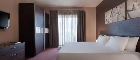 A hotel room with a large bed, a wardrobe, a flat-screen TV, and a window with curtains.