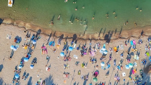Vista aérea de una playa con gente tomando el sol y nadando, sombrillas y sillas de playa.
