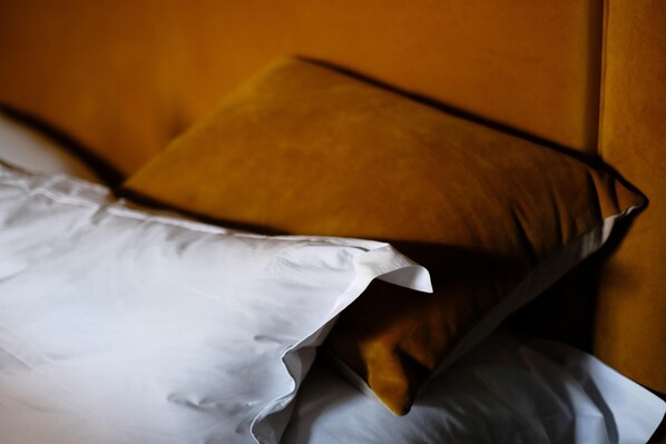 Una cama con sábana blanca y dos almohadas, una de color marrón oscuro.