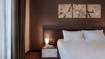 Una habitación de hotel con una cama bien hecha, una mesita de noche con una lámpara y una planta pequeña, y tres cuadros en la pared.