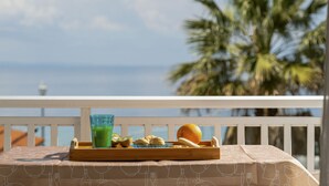 Ein Tisch mit einer Platte voller Speisen und Getränken auf einem Balkon mit Blick auf den Ozean und Palmen.