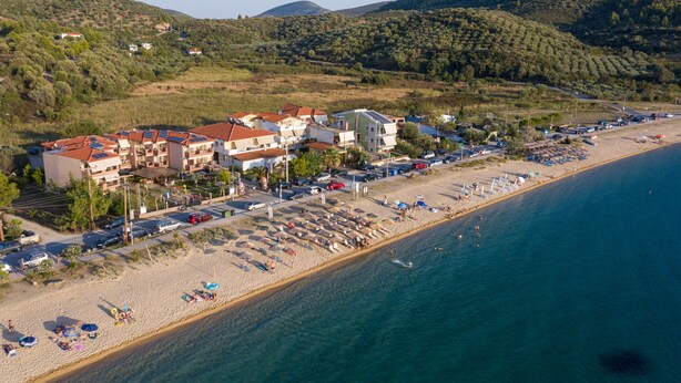 Ein Küstenhotel mit mehreren Gebäuden, ein Strand mit Liegestühlen und freier Meersicht.