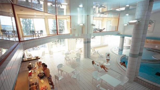 Un área de piscina interior espaciosa con varias zonas de estar y una piscina central.