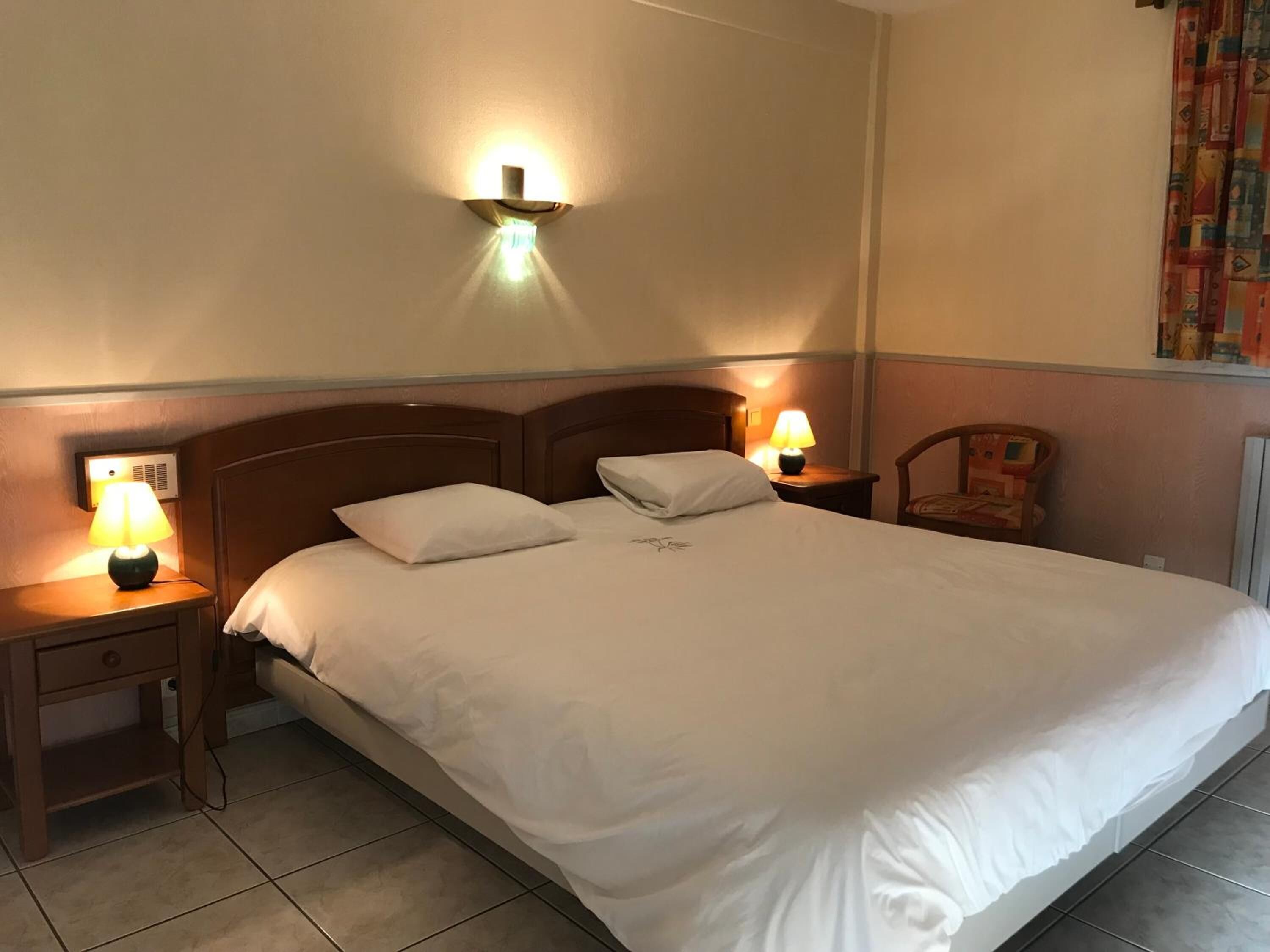 Habitación de hotel con una cama grande, dos mesitas de noche con lámparas, un cabecero de madera y una lámpara fijada a la pared.