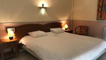 Habitación de hotel con una cama grande, dos mesitas de noche con lámparas, un cabecero de madera y una lámpara fijada a la pared.