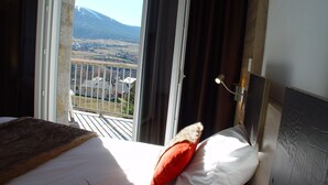 Una habitación de hotel con una cama, una ventana con cortinas y vistas a un paisaje montañoso.
