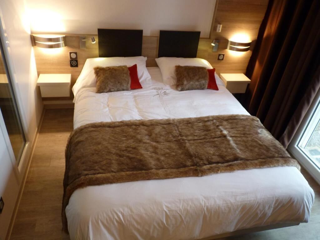 A hotel room with a large bed, two bedside tables, a headboard, and a window with curtains.