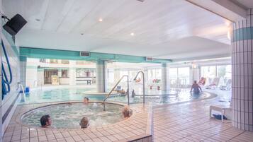 An indoor swimming pool with multiple hot tubs and lounge areas.