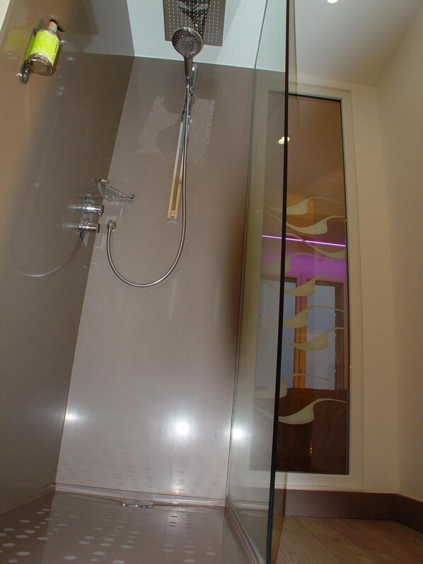 A modern bathroom with a glass shower enclosure, a handheld showerhead, and a wall-mounted faucet.