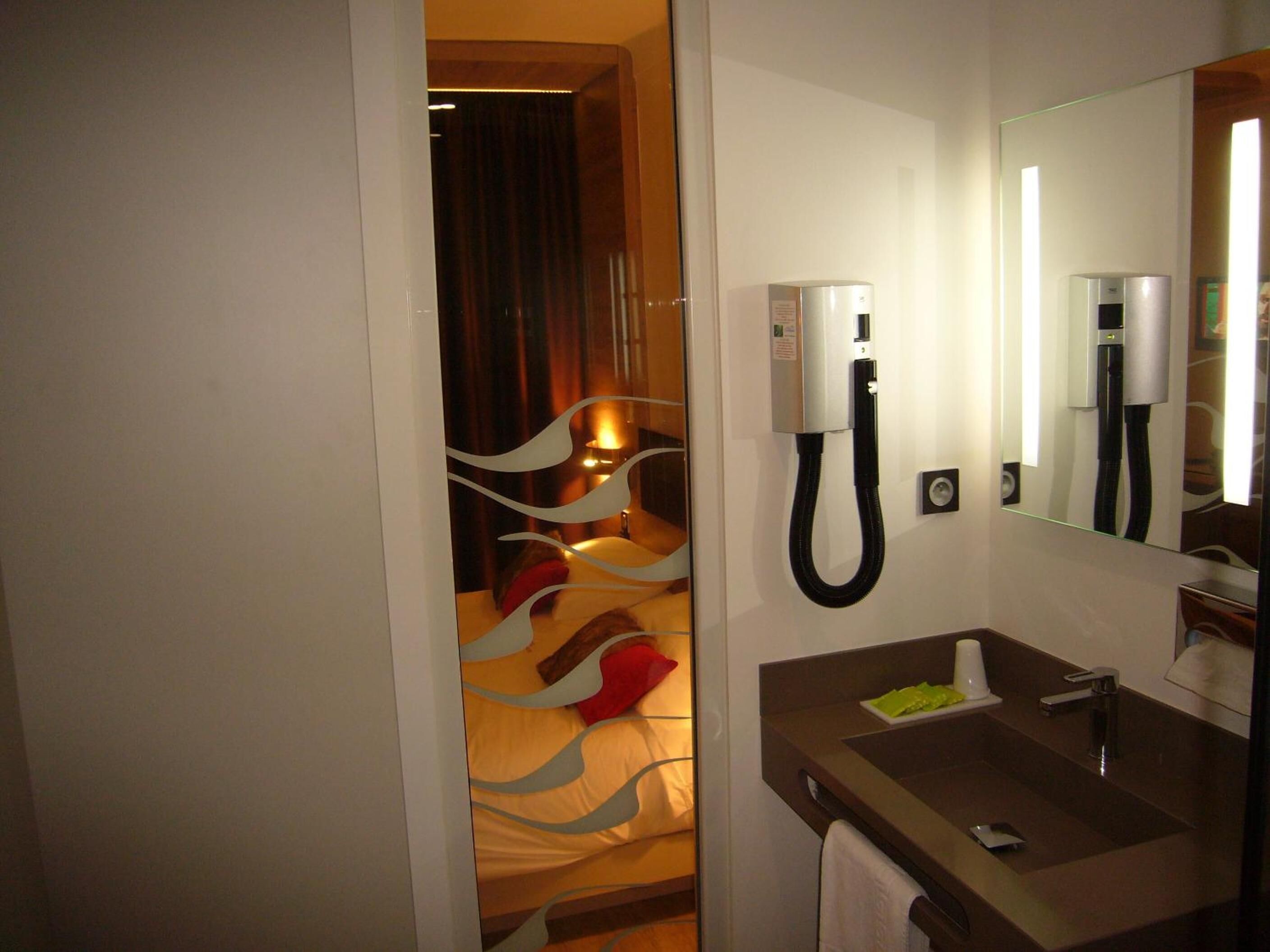 A hotel room with a bed, a bedside table, a mirror, a sink, and a telephone.