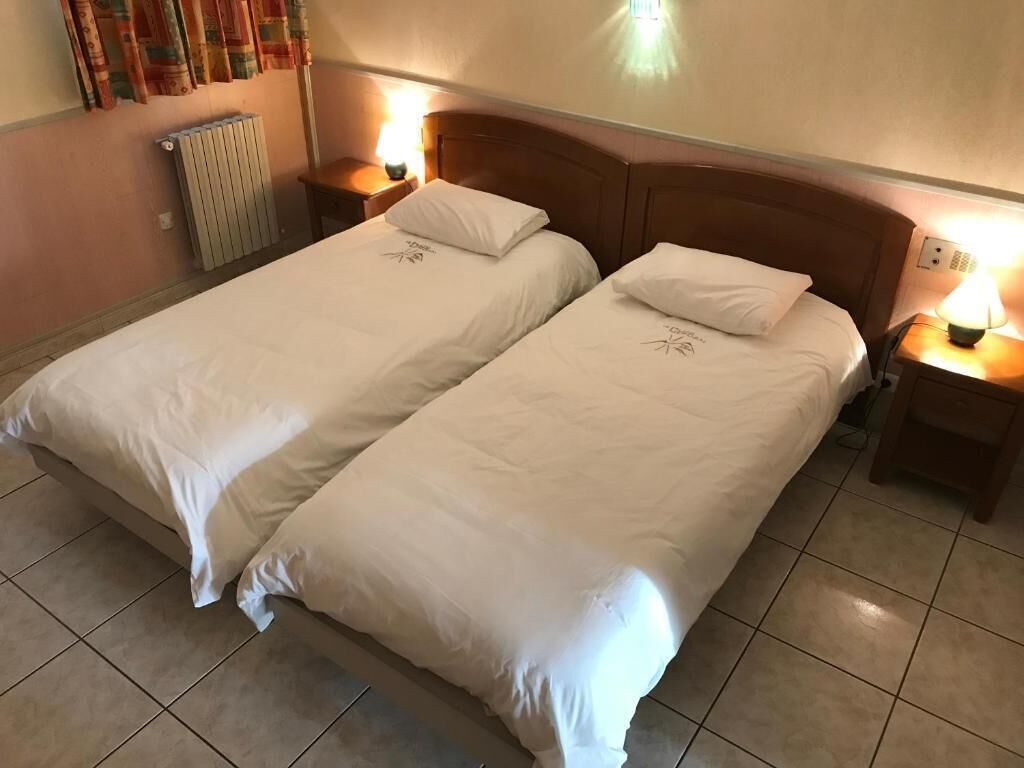 A double bed with white bedding, two bedside tables with lamps, a radiator, and a wall with curtains.