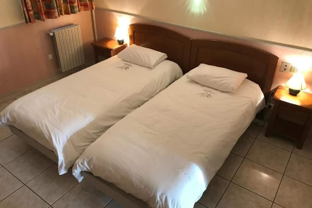 A double bed with white bedding, two bedside tables with lamps, a radiator, and a wall with curtains.