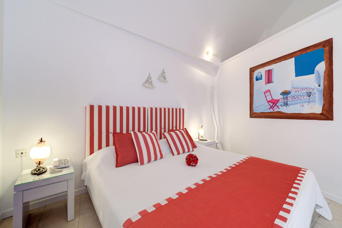 A neatly made bed with striped bedding, a bedside table with a lamp, and a framed picture on the wall.