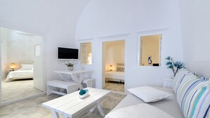 Una habitación moderna con una decoración en tonos blancos, una cama, una mesa blanca con un cuenco, un televisor montado en la pared y un sofá a rayas.