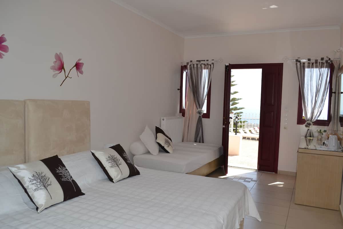 A bedroom with two beds, a wooden desk, and a view of the beach through an open door.