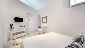 A modern bedroom with a large bed, a TV mounted on the wall, a small white bench, and a potted plant.