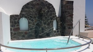 Un hidromasaje de paredes de piedra con barandilla metálica, frente a una pared blanca con un arco de piedra.