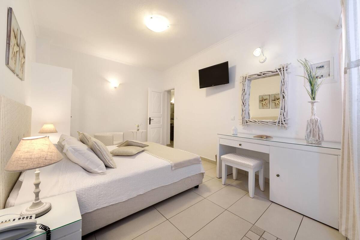 A bedroom with a bed, bedside table, lamp, TV, dresser, and a mirror.
