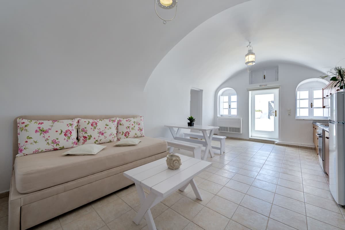 A spacious living area with a sofa, a coffee table, and a dining table. There are white walls and a high ceiling with a skylight.