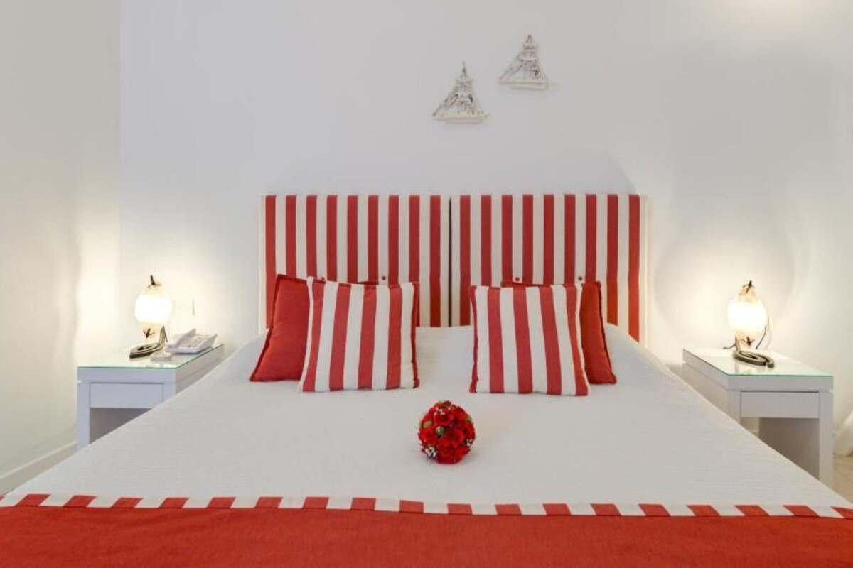 A bed with red and white striped bedding, two bedside tables with lamps, and a red flower centerpiece.