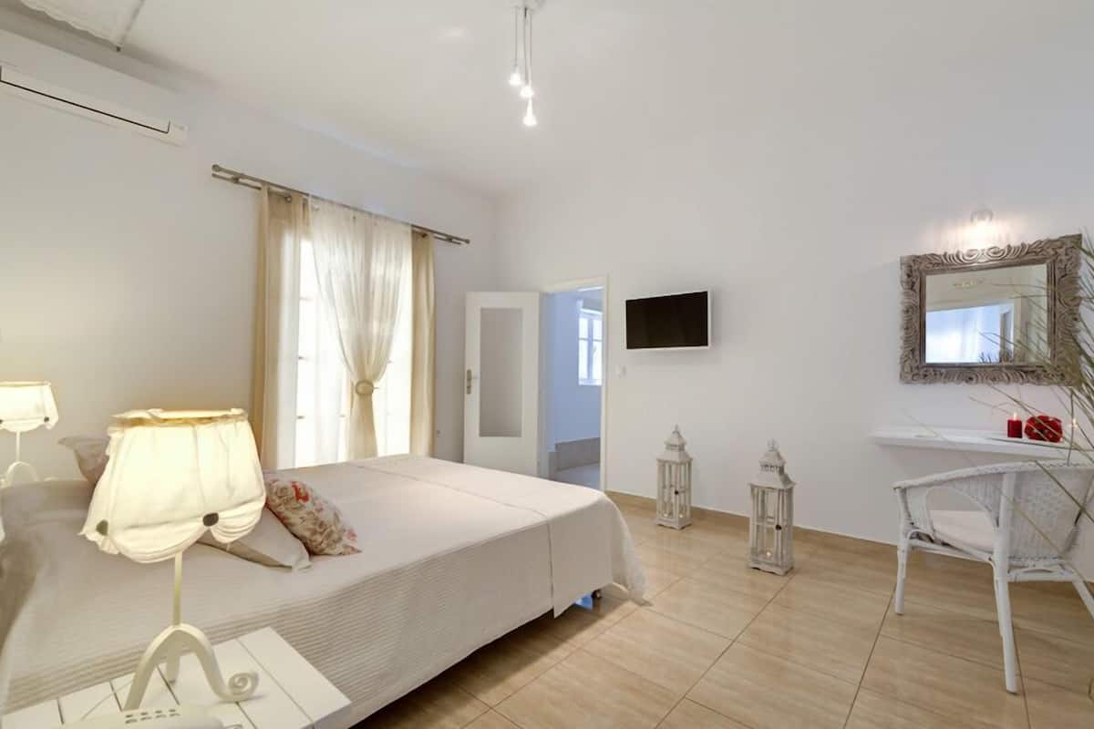 A bedroom with a bed, bedside lamps, a desk with a chair, a mirror, and a TV.