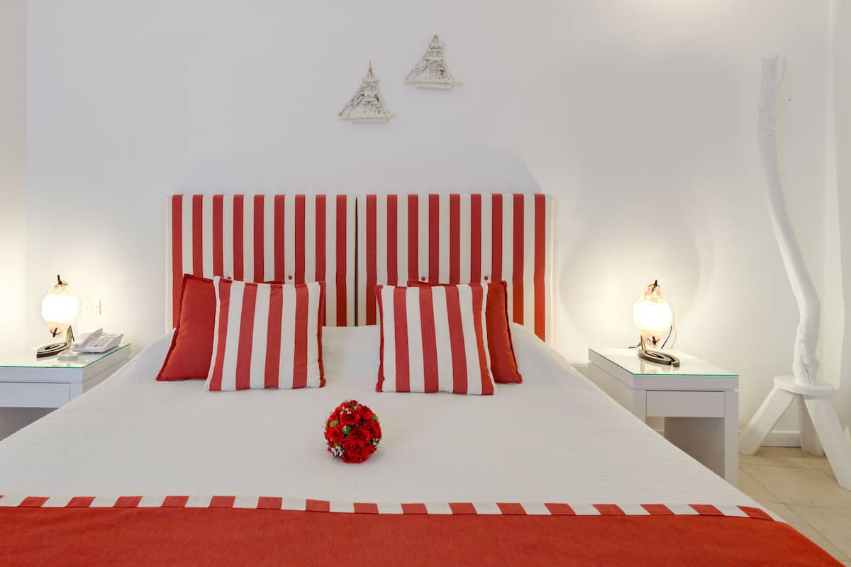 A hotel room with a striped headboard, a bed with red and white bedding, a bouquet of red roses, and two bedside tables with lamps.