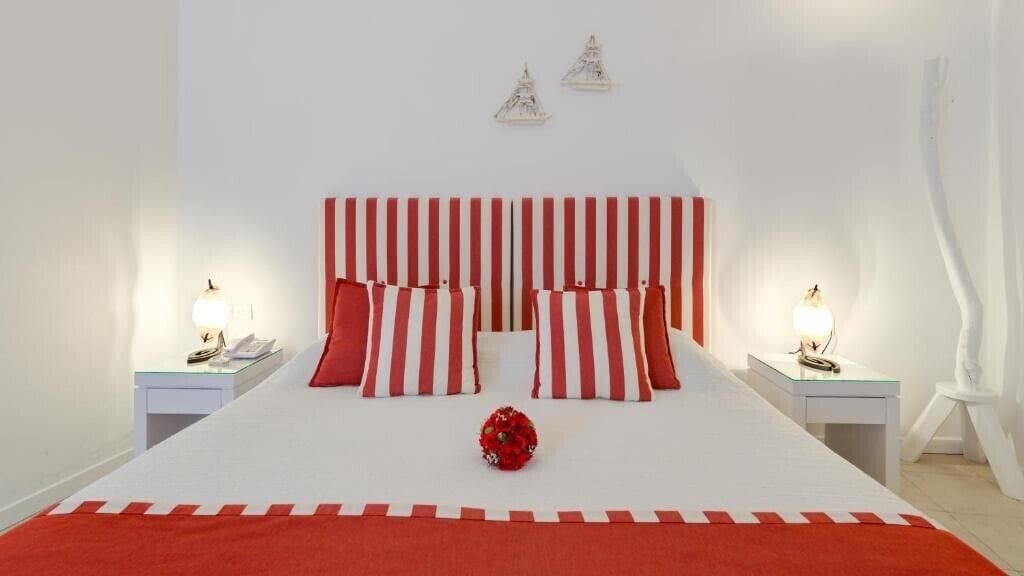 A bed with red and white striped bedding, two bedside tables with lamps, and a red flower centerpiece.
