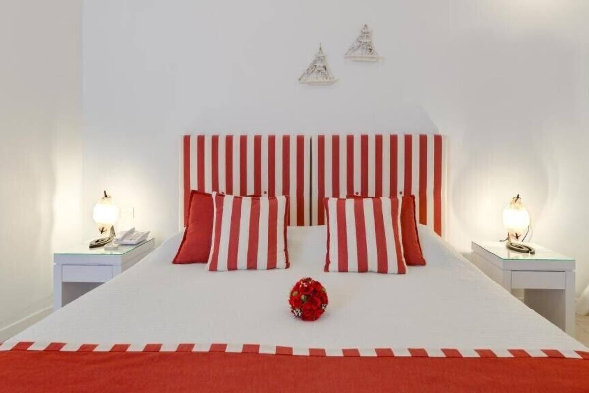 A bed with red and white striped bedding, two bedside tables with lamps, and a red flower centerpiece.