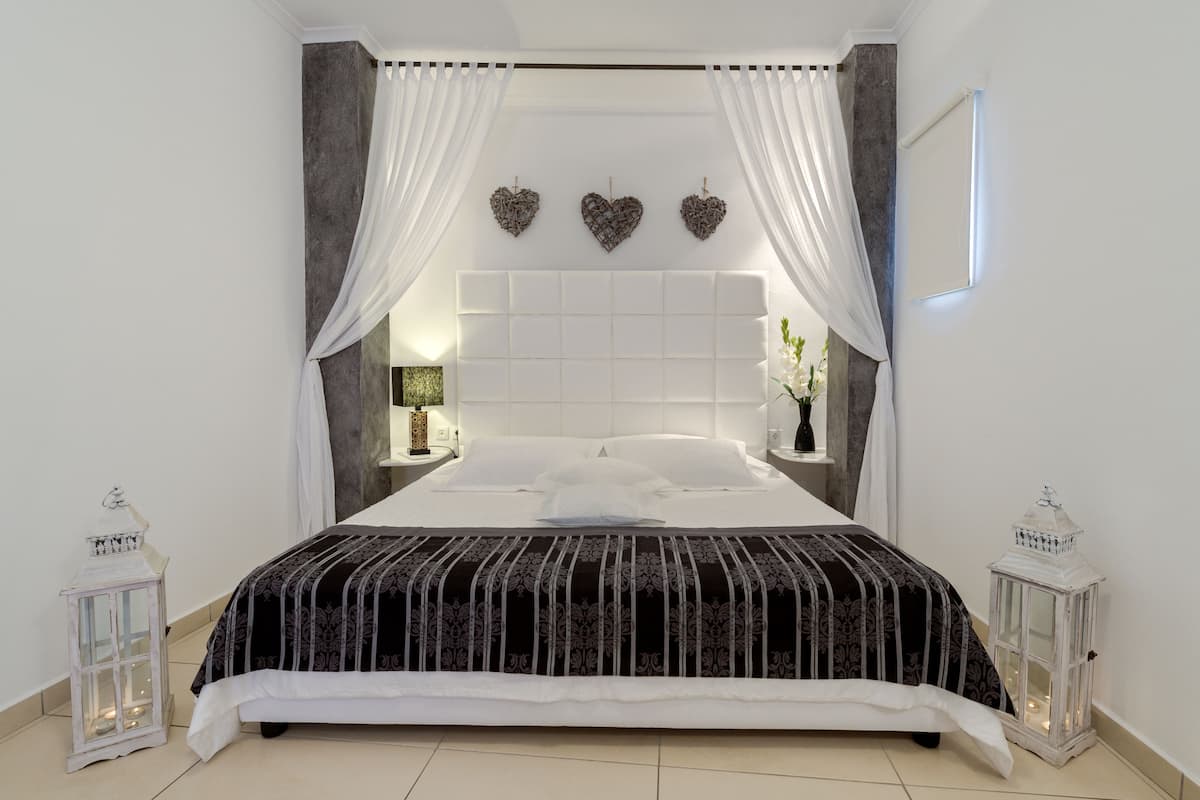 A neatly made bed with a patterned bedspread, white curtains, and decorative heart-shaped wall hangings.
