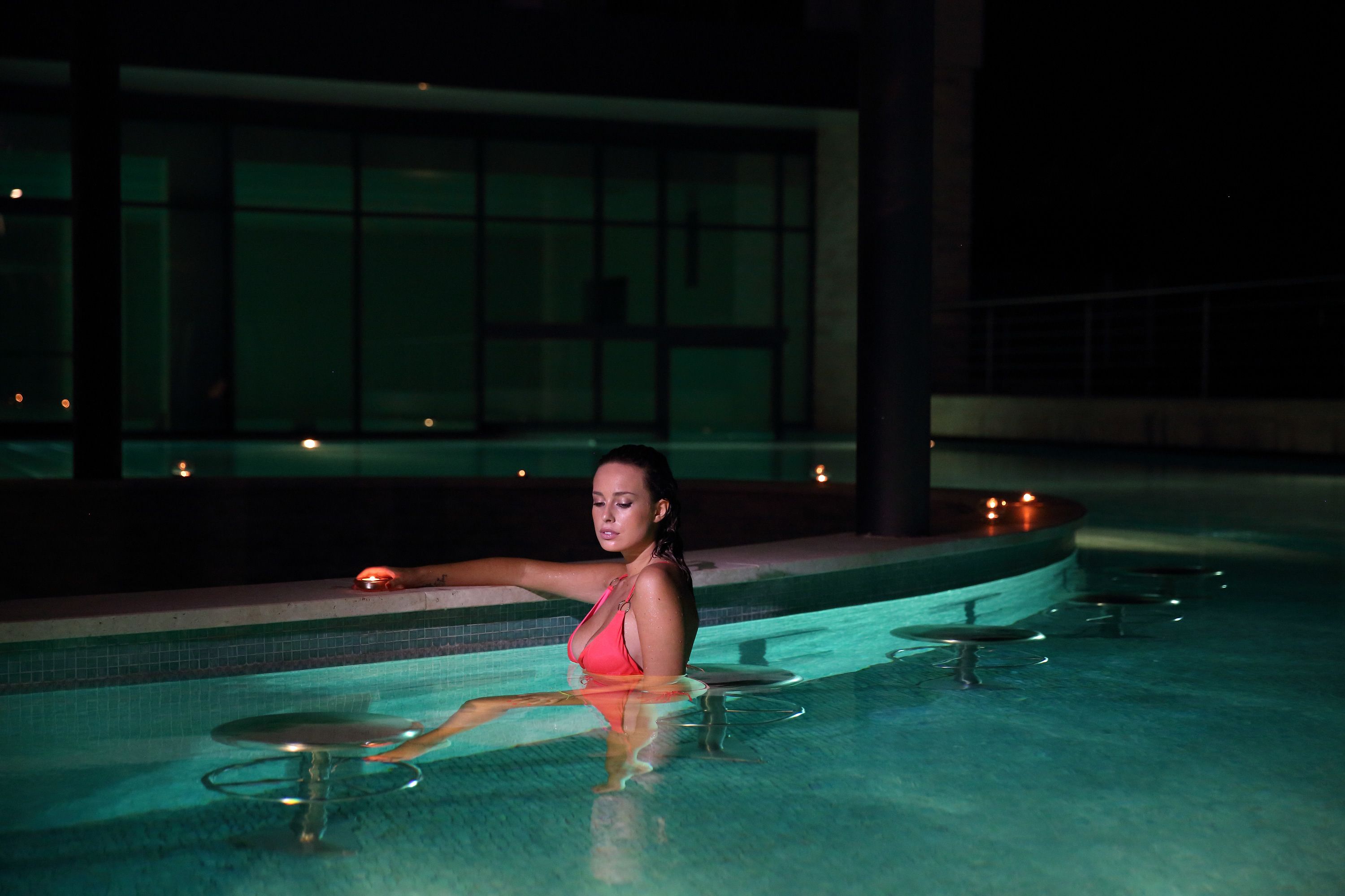 Mulher sentada à beira da piscina, com uma mesa em primeiro plano.