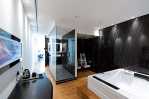 A modern bathroom with a large bathtub, a glass shower enclosure, and a wooden floor.