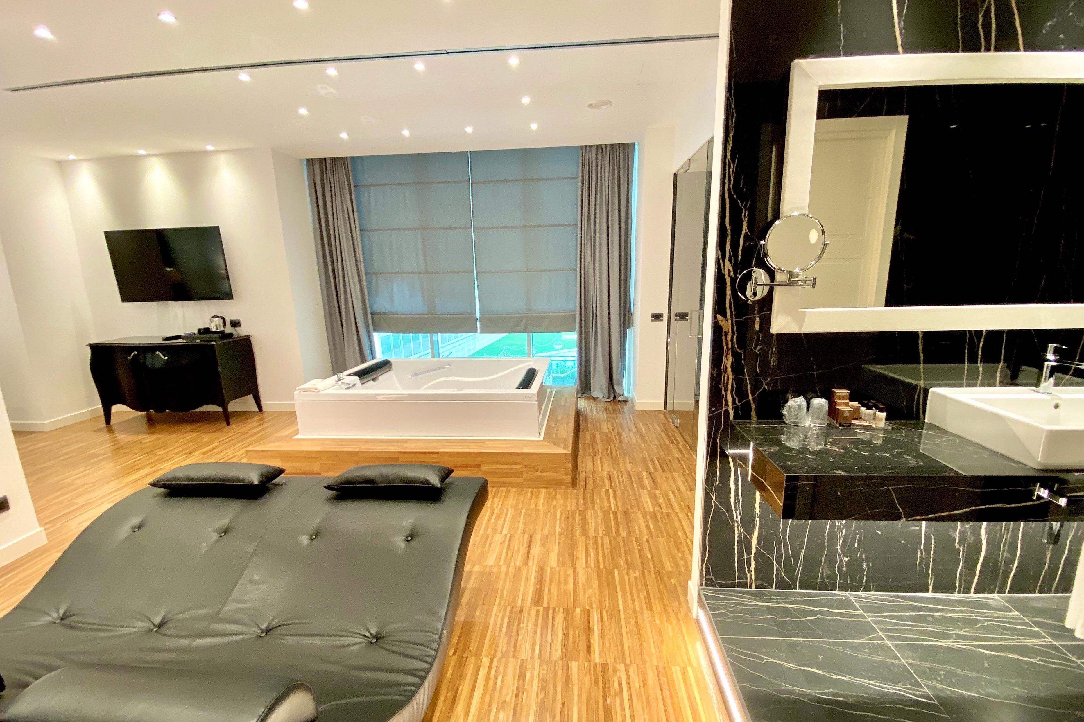 Una camera d'albergo moderna con un letto grande, un lettino per massaggi, una televisione e un bagno con specchio e lavandino.