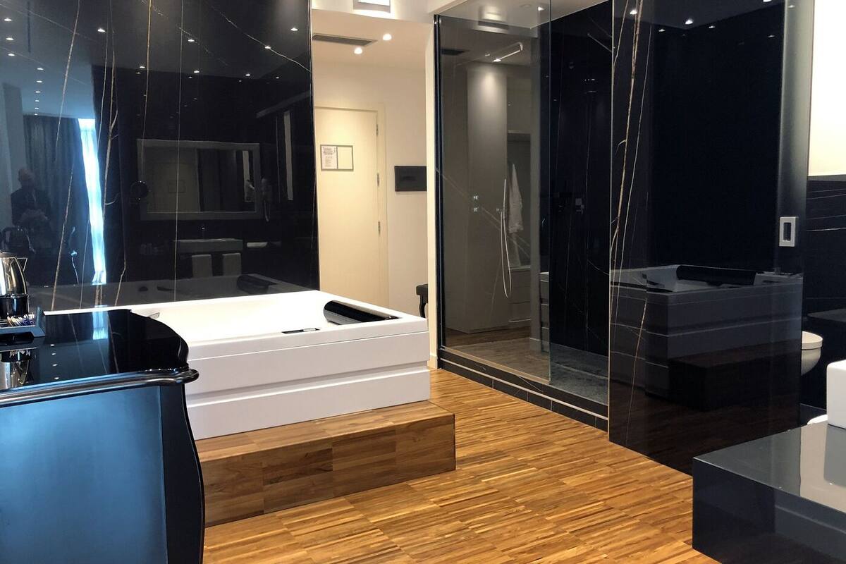 A modern bathroom with a large mirror, a white bathtub, and a glass-enclosed shower area.