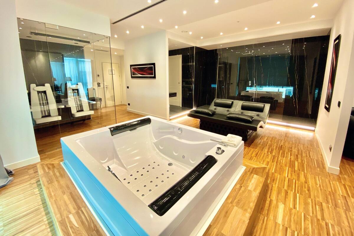 A modern bathroom with a large bathtub, wooden flooring, and a glass shower enclosure.