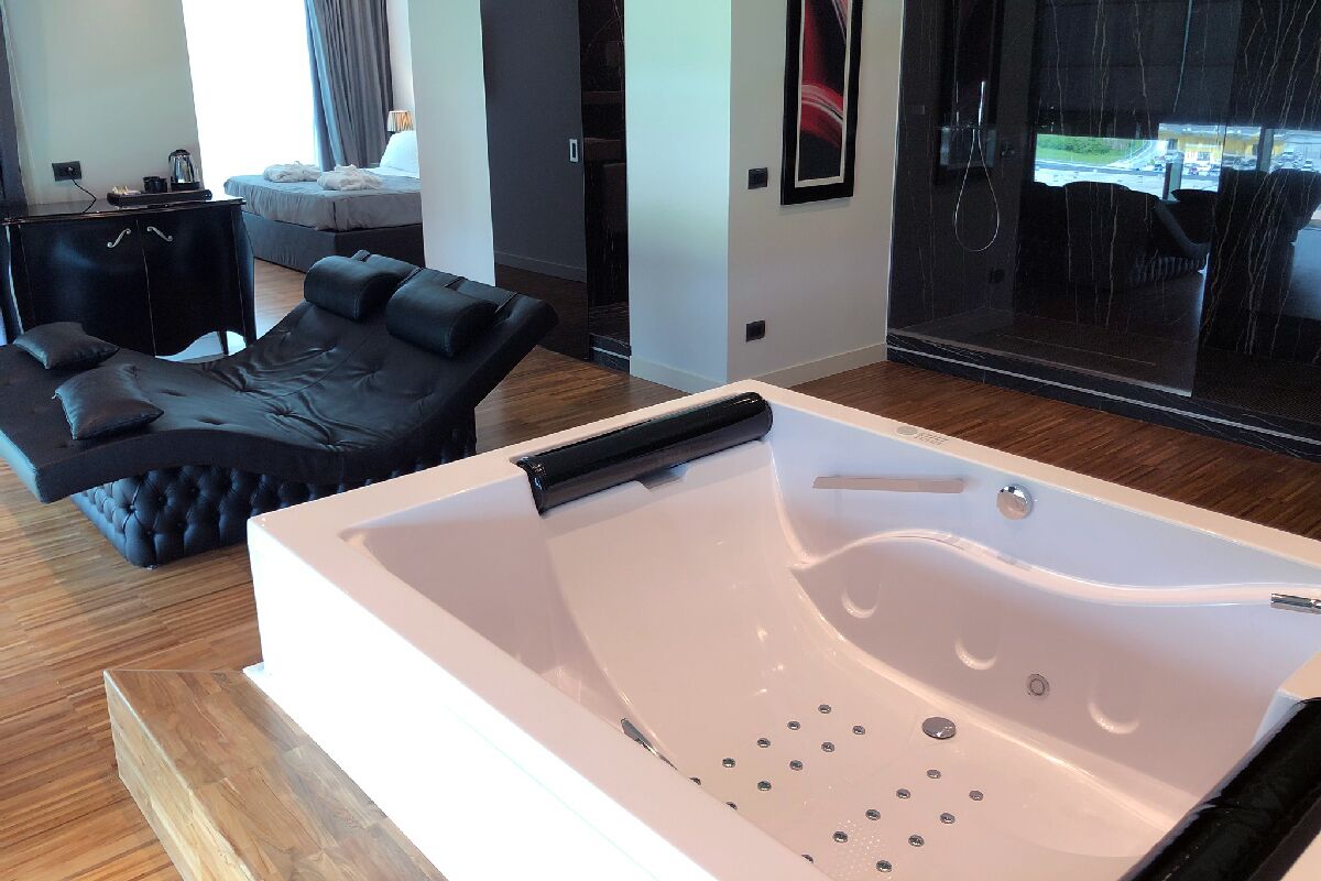 Una habitación moderna con una bañera blanca grande, un sofá de cuero negro y una zona de comedor con vistas al exterior.