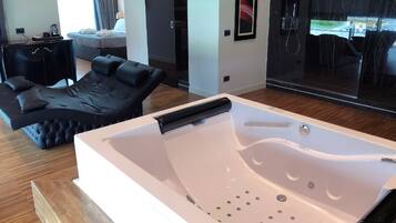 Una habitación moderna con una bañera blanca grande, un sofá de cuero negro y una zona de comedor con vistas al exterior.