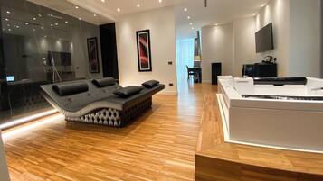A modern hotel room with a large bed, a white console table, a flat-screen TV, and a large window offering a view of the city.